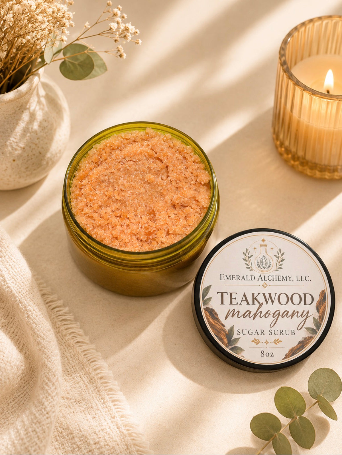 Teakwood Mahogany Sugar Body Scrub 8 oz with open scrub, labeled lid, candle, and eucalyptus